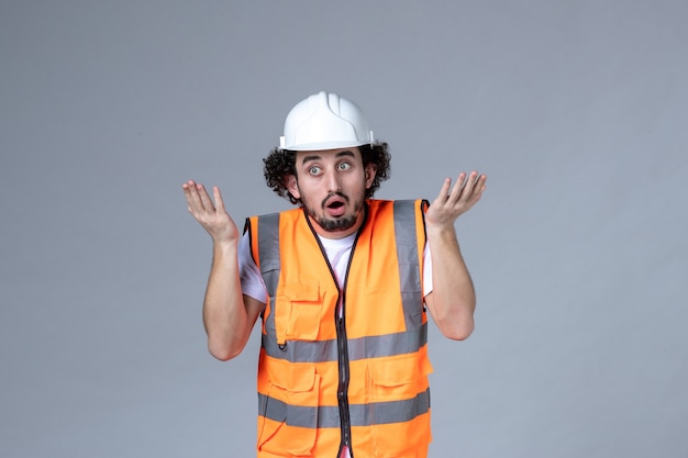 Front view of wondering male builder wearing warning vest with safety helmet on gray wave wall