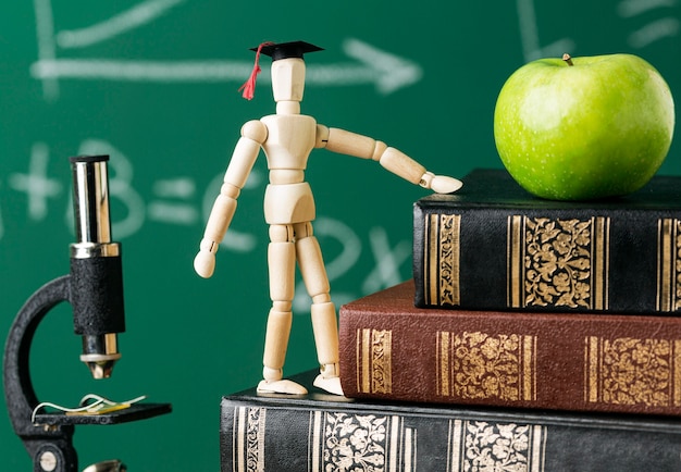 Free photo front view of wooden figurine with academic cap and apple