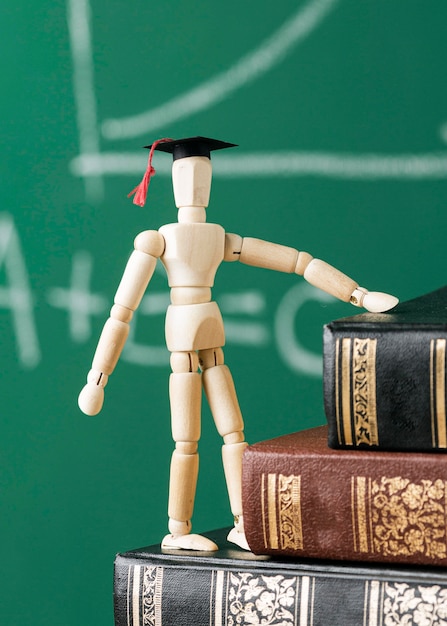 Front view of wooden figurine with academic cap and stack of books