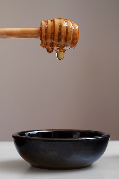 Front view of wooden honey dipper with honey and bowl