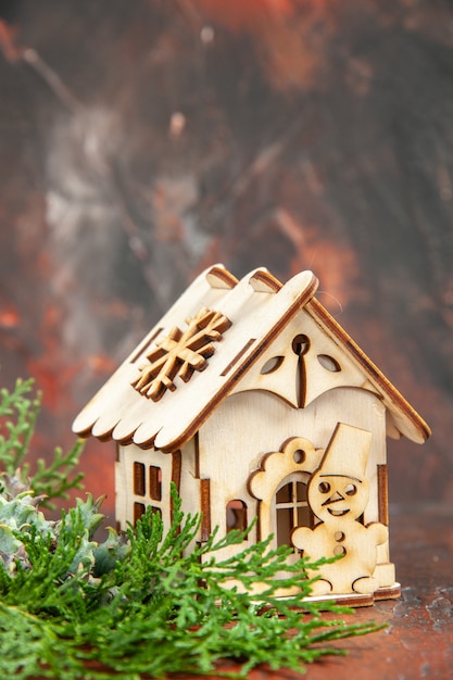 Бесплатное фото Вид спереди деревянный игрушечный домик сосновые ветки на темно-красном столе свободное пространство