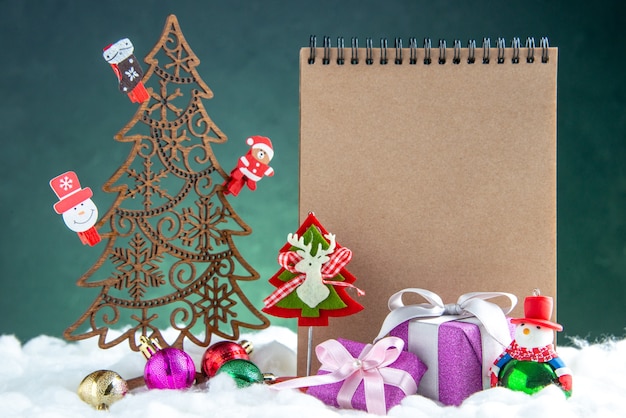 Бесплатное фото Вид спереди деревянная рождественская елка с игрушками, блокнот из сосновой шишки, небольшие подарки