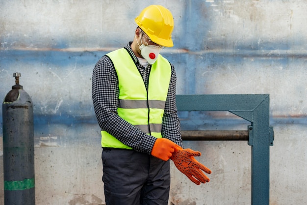 Front view of worker with hard hat putting on protective gloves