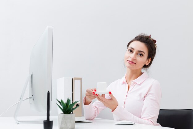 Front view of working woman holding cup of coffee at desk