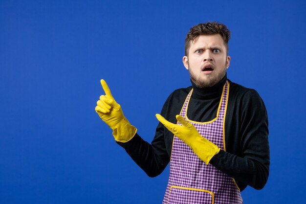 Front view of worried male housekeeper in black sweater standing on blue isolated wall