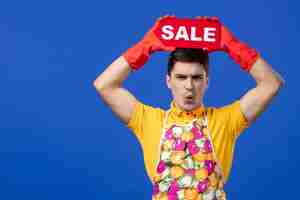 Free photo front view of worried male housekeeper in yellow t-shirt raising sale sign over his head on blue wall