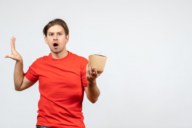 Front view of worried young guy in red blouse holding small box on white background