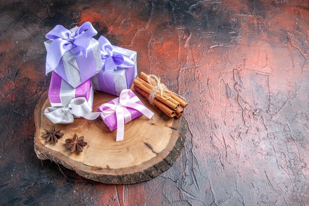 Front view xmas gifts anises cinnamon on tree cutting board on dark red background with free space