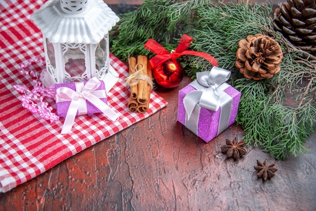 Front view xmas gifts pine tree branches with cones xmas ball toy lantern red tablecloth on dark red background xmas photo