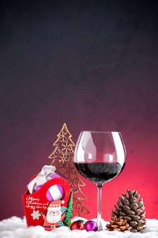 Vista frontale regali di natale bicchiere di vino pigna su sfondo rosso