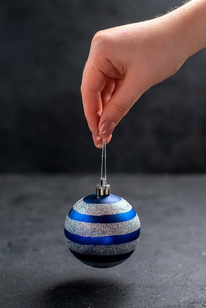 Front view xmas tree ball in female hand on dark isolated background