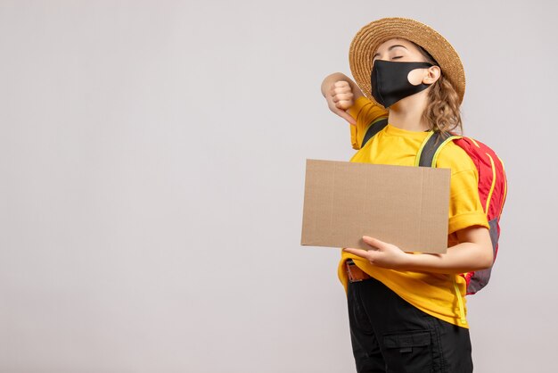 Front view yawning female traveller with backpack holding cardboard