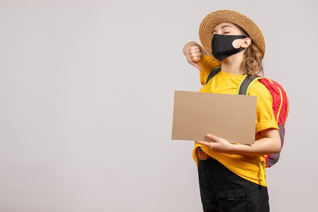 Front view yawning female traveller with backpack holding cardboard