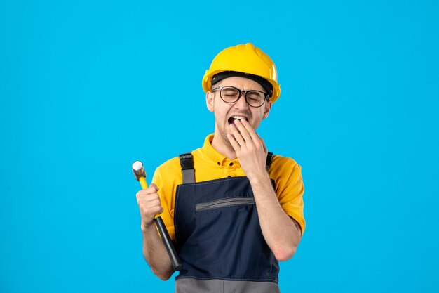 Front view of yawning male worker in yellow uniform on a blue 