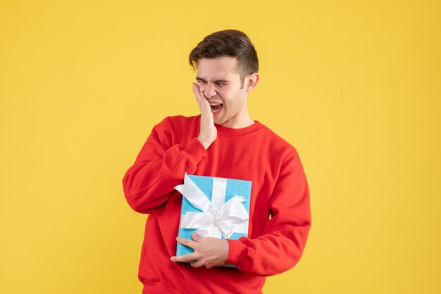 Front view yawning young man with red sweater standing on yellow background