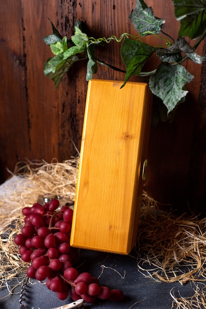 A front view yellow box closed along with red grapes and green leaves on the brown background winery fruits berries