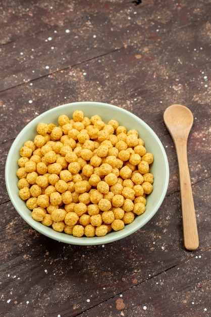 Cereali gialli di vista frontale dentro il piatto su legno scuro, alimento dei cereali dei fiocchi di granturco della prima colazione