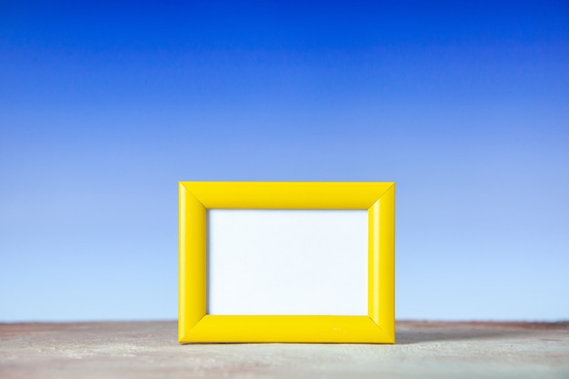 Free photo front view of yellow empty picture frame standing on table on white and blue surface with free space