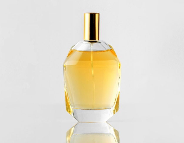 A front view yellow fragrance in bottle with golden cap on the white wall