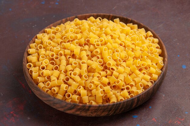 Вид спереди желтая итальянская паста в сыром виде на темном столе