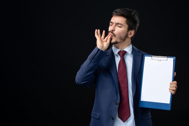 Front view of young adult in suit holding free space for writing and making perfect gesture on isolated dark wall