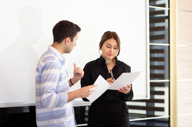 Free photo a front view young attractive businesswoman in black shirt along with young man discussing graphics on the desk while young lady presents her work reading document job building presentation