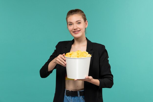 Front view young attractive female in black jacket holding cips on blue surface