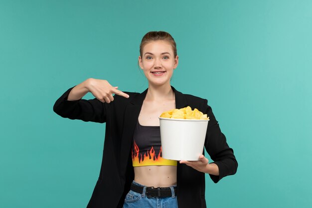 Front view young attractive female in black jacket holding cips on the blue surface