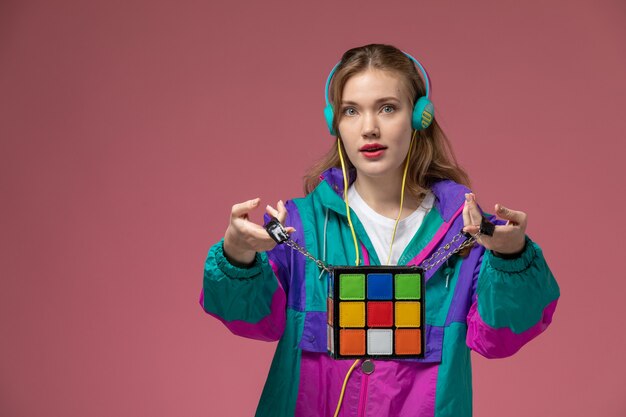 Front view young attractive female in colored coat listening to music holding funny bag on the dark-pink wall model color female young girl