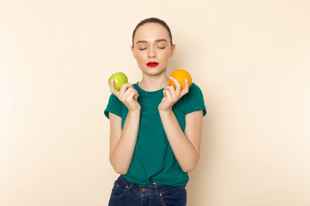 Front view young attractive female in dark green shirt holding orange and apple on beige