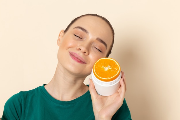 Front view young attractive female in dark green shirt holding orange on beige