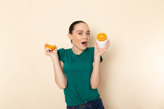Front view young attractive female in dark green shirt holding orange rings on beige