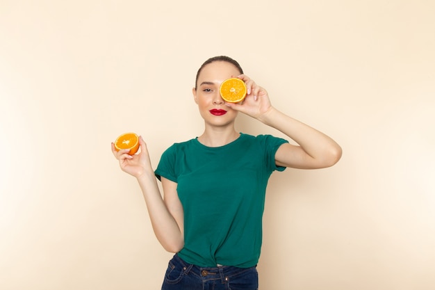 Front view young attractive female in dark green shirt holding oranges on beige