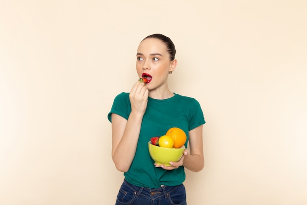 과일 접시를 들고 진한 녹색 셔츠에 전면보기 젊은 매력적인 여성
