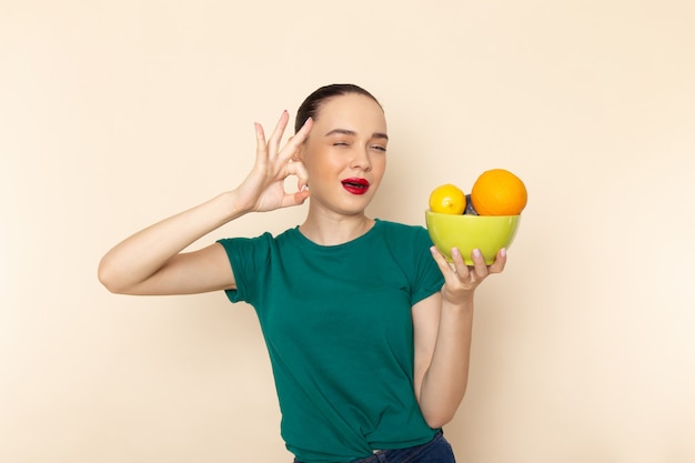 果物とプレートを保持している濃い緑のシャツの正面若い魅力的な女性
