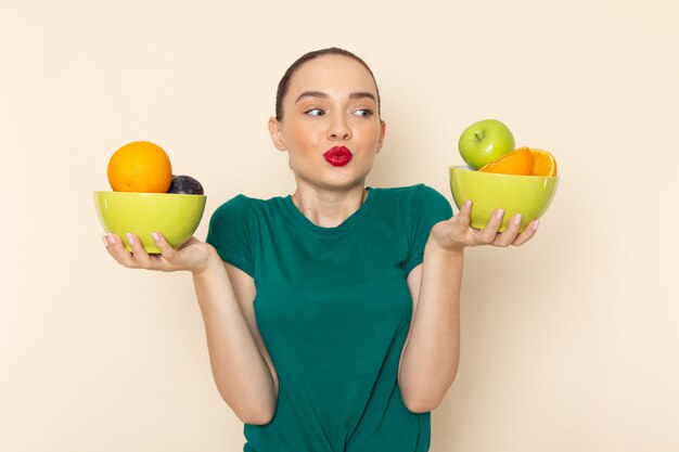 Front view young attractive female in dark green shirt holding plates with fruits