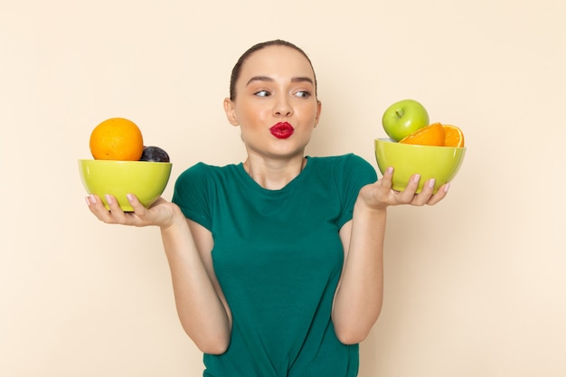 果物とプレートを保持している濃い緑色のシャツで正面の若い魅力的な女性
