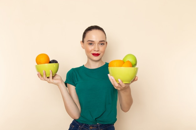 Front view young attractive female in dark green shirt holding plates with fruits