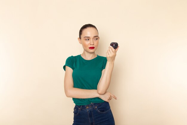 Front view young attractive female in dark green shirt holding plum on beige