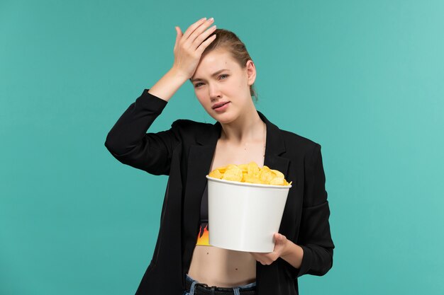 Front view young attractive female holding cips and watching movie on light-blue surface