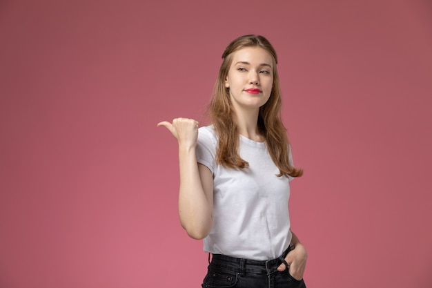 ピンクの壁のモデルの色の若い女性に笑顔でポーズをとる白いtシャツの正面のクローズビュー若い魅力的な女性 無料の写真