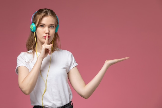 Вид спереди молодая привлекательная женщина, слушающая музыку и показывающая знак тишины на розовой стене цвет модели женщина молодая девушка