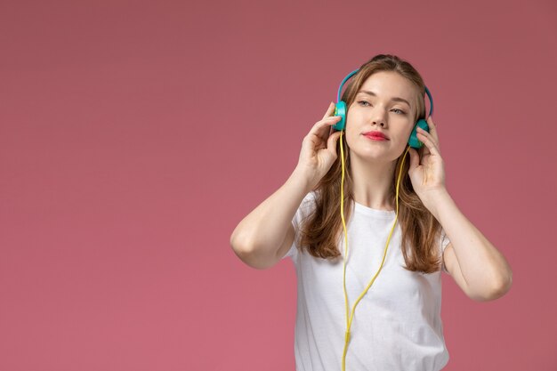 Вид спереди молодая привлекательная женщина, слушающая музыку через наушники на темно-розовой стене, цвет модели женщина молодая девушка