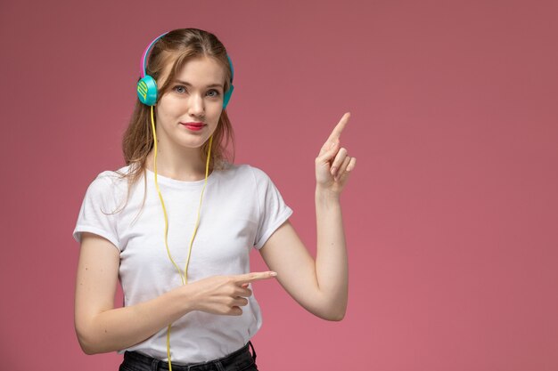 Front view young attractive female listening to music via her earphones with slight smile on dark-pink wall model color female young girl