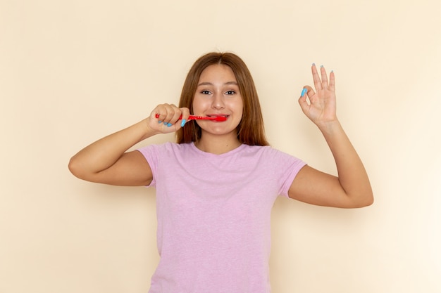 Front view young attractive female in pink t-shirt and blue jeans cleaning her teeth with smile