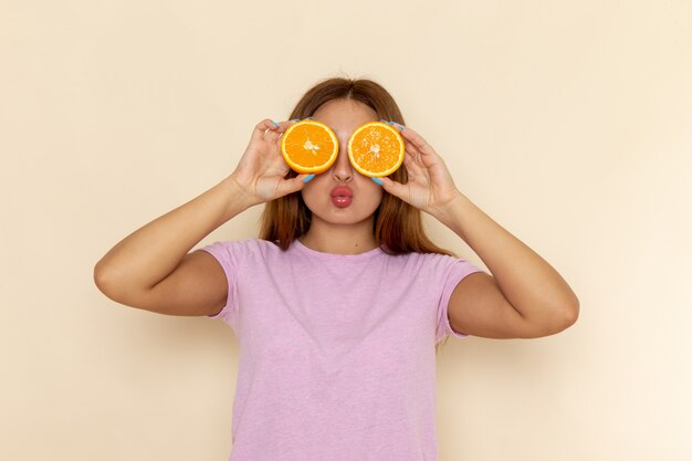 Вид спереди молодая привлекательная женщина в розовой футболке и синих джинсах, закрывающая глаза апельсинами