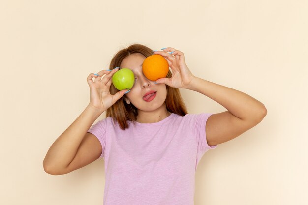 Front view young attractive female in pink t-shirt and blue jeans holding apple orange and posing with smile