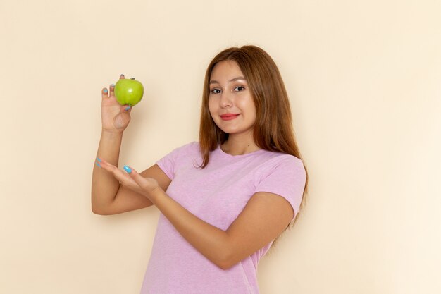 Front view young attractive female in pink t-shirt and blue jeans holding fresh green apple