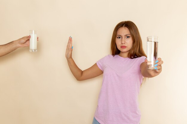 Front view young attractive female in pink t-shirt and blue jeans holding glass of water and denying milk