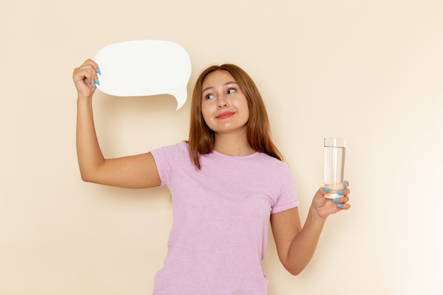 ピンクのtシャツとブルージーンズの水と白い看板のガラスを保持している正面の若い魅力的な女性